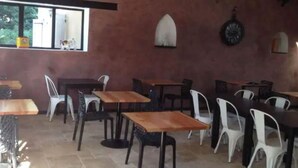 Ein Restaurant mit mehreren Tischen und Stühlen, einem Fenster mit Blick auf Bäume und einer rustikalen Einrichtung mit sichtbaren Holzbalken.