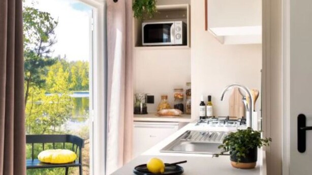Eine moderne Küche mit eingebauter Mikrowelle, einem Spülbecken und einer kleinen Kochinsel mit einer Zitrone. Vor dem Fenster steht ein Stuhl und auf der Arbeitsplatte ein Blumentopf.