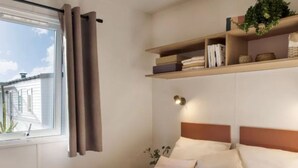Ein Schlafzimmer mit einem Bett, einem Fenster mit Vorhängen, einem Regal mit Büchern und Dekoration sowie einer Wandleuchte.