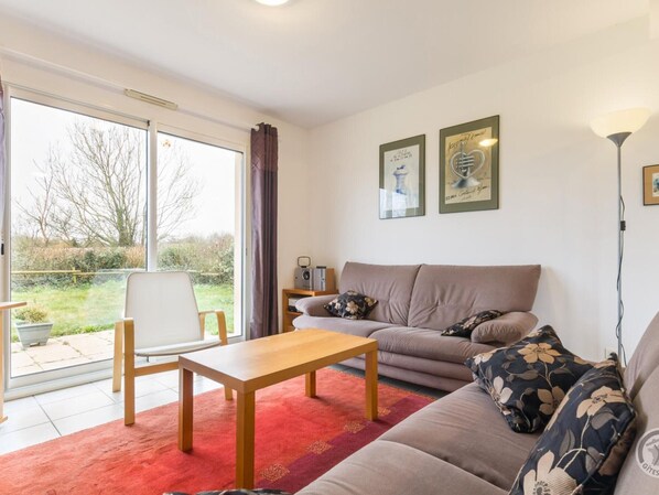 A living room with a sofa, a wooden coffee table, and a red rug. There is a window with a view of the outdoors. - House with pets allowed, parking - 6 guests (La Feuillie)