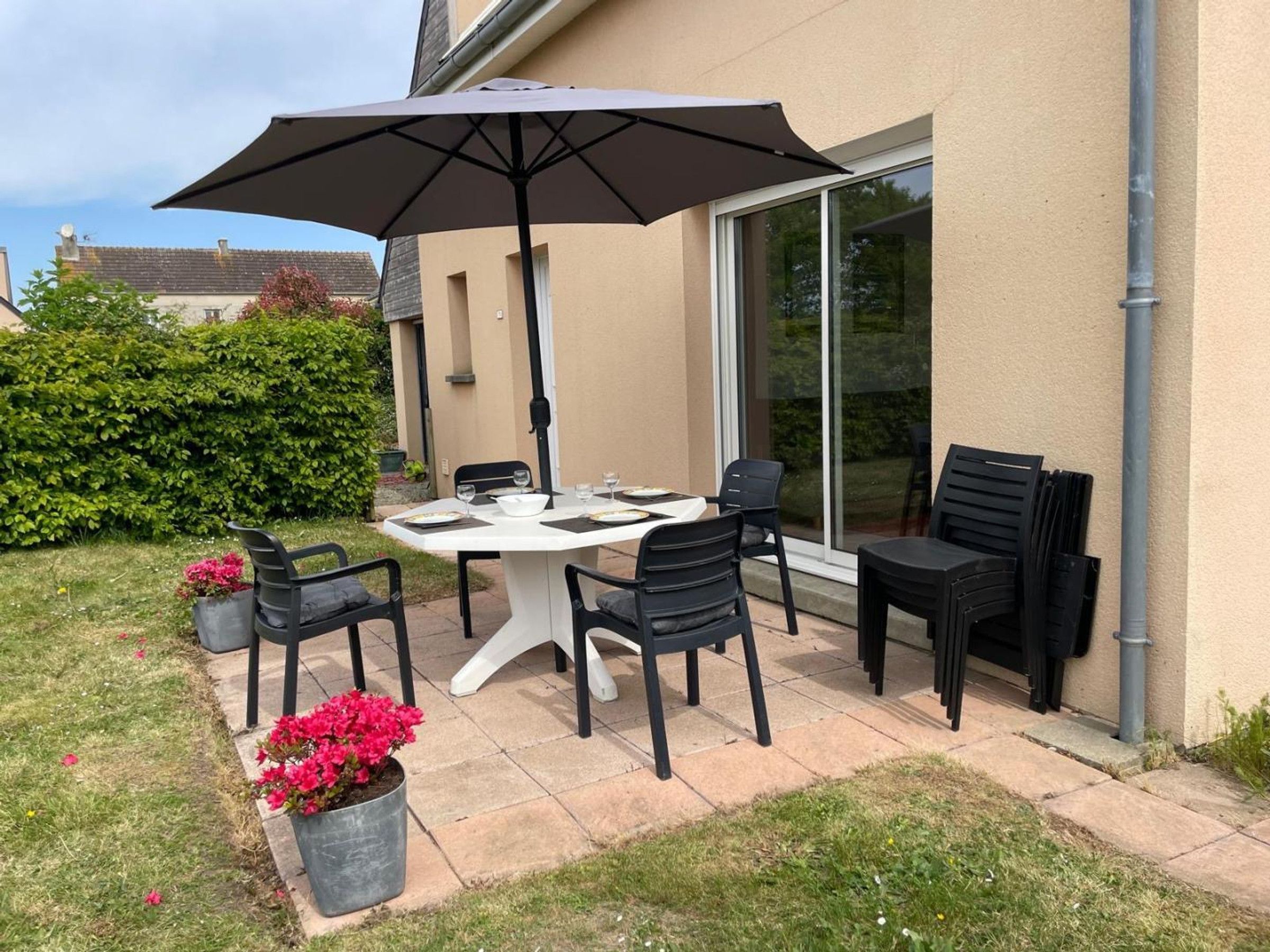 An outdoor patio with a table and chairs, a large umbrella, and potted plants.