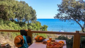 Ein Tisch mit Obstkorb, Croissants und einem Getränk auf einer Holzterrasse mit Blick aufs Meer.