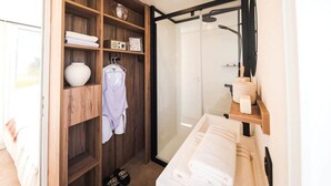 Ein modernes Badezimmer mit einer Duschkabine aus Glas, einem Holzausleger mit Spiegel und einer eingebauten Ablage mit Handtüchern und Pflegeartikeln.