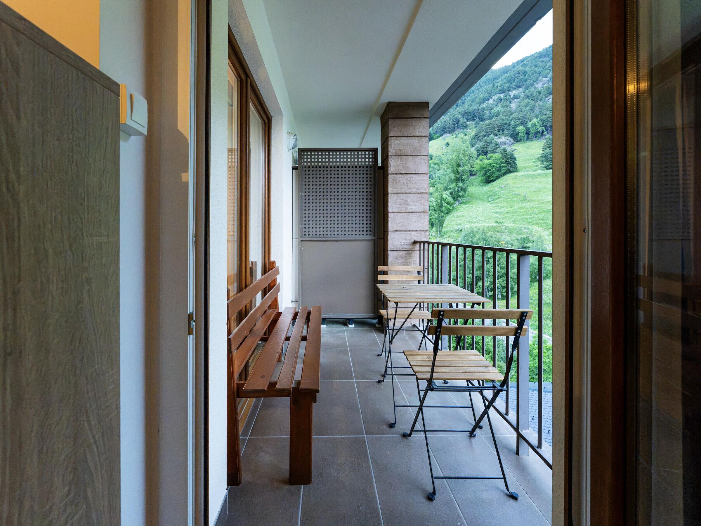 Un balcone con una panchina e tavoli di legno, vista su un paesaggio verde e un muro in pietra.