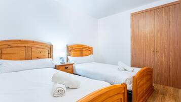 A hotel room with two wooden beds, a nightstand with a lamp, and a wooden wardrobe.