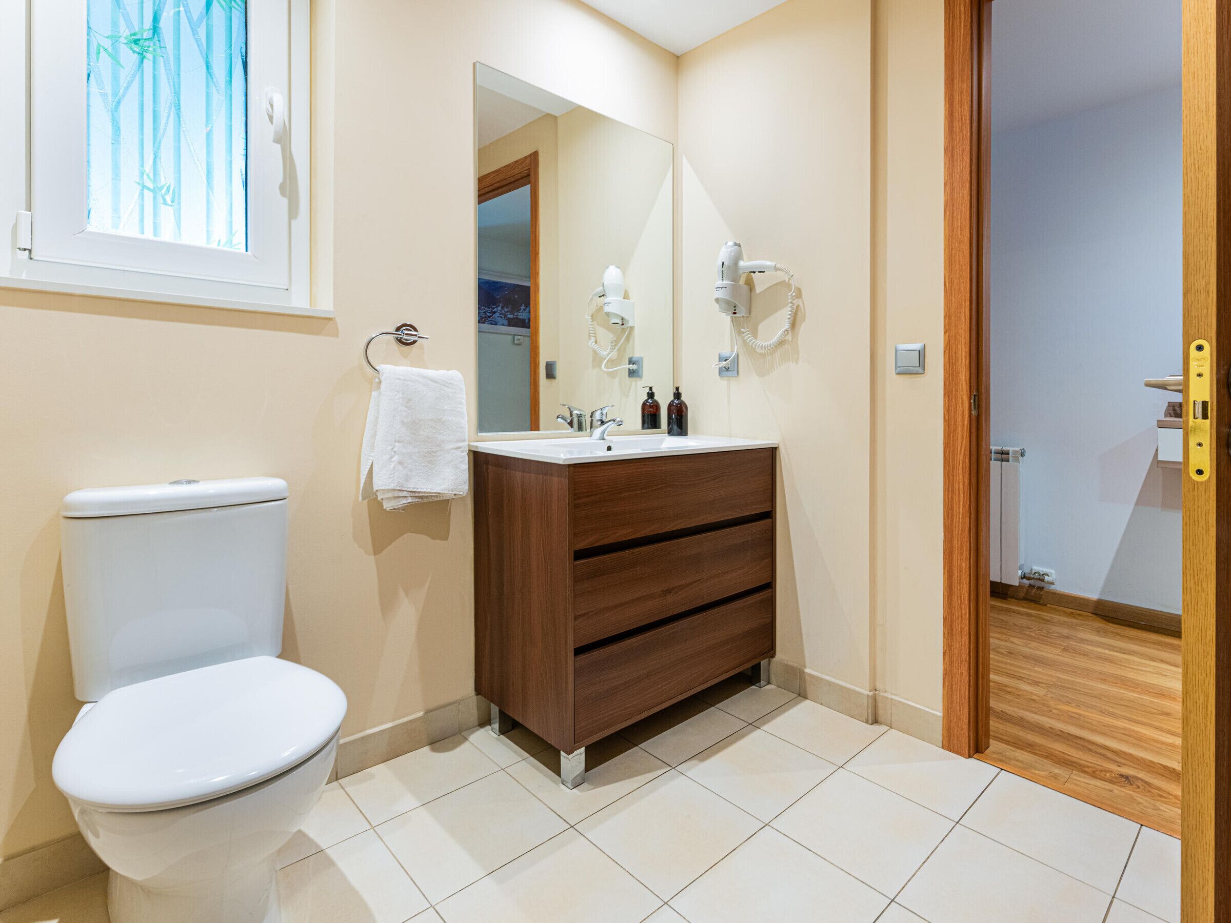 Un baño con inodoro, lavamanos con espejo y un armario de madera.