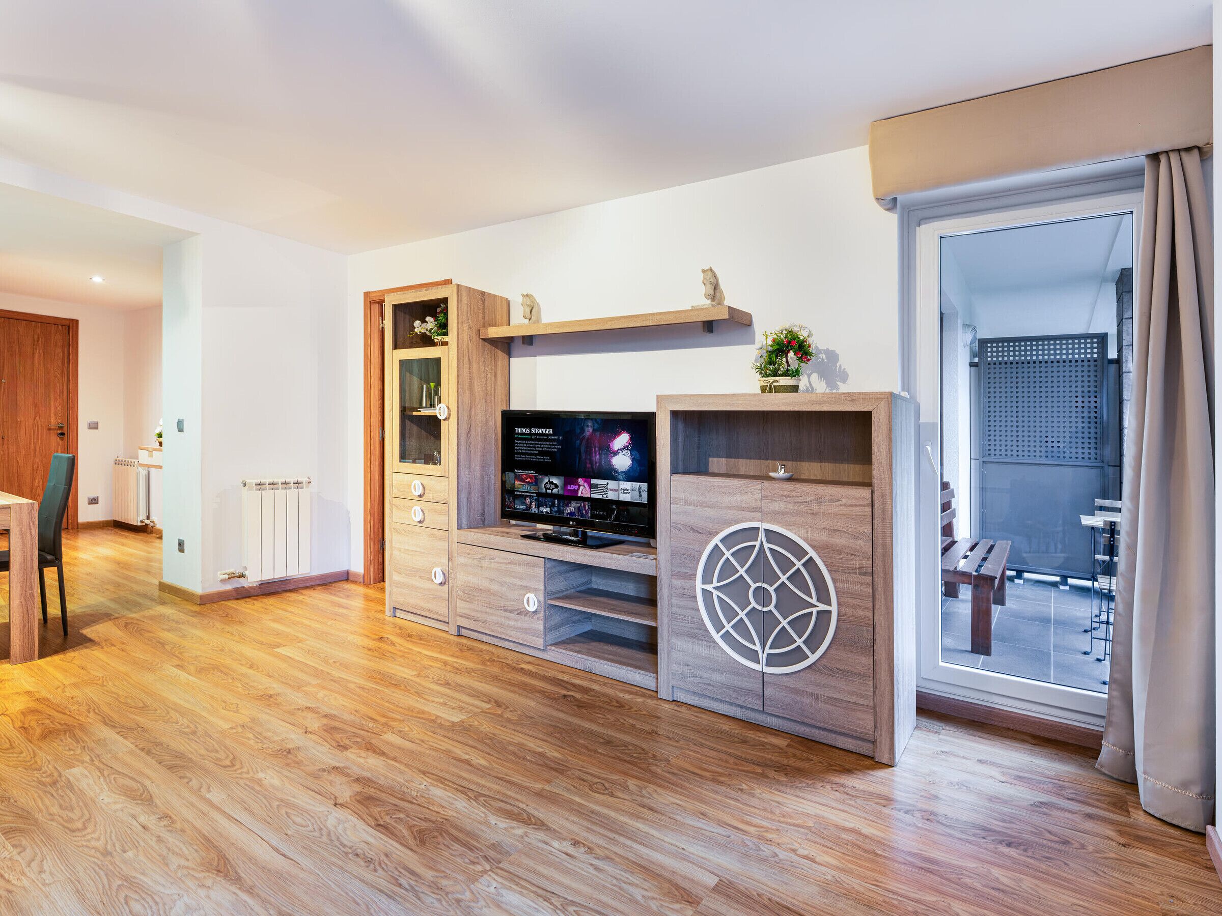 A modern living room with a wooden entertainment unit, a television, and a sliding glass door leading to an outdoor area.