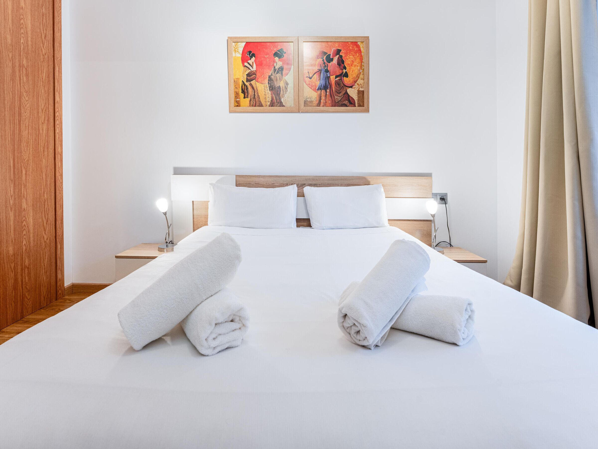 Habitación de hotel con una cama bien hecha, dos lámparas de noche y un cuadro en la pared.