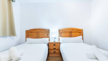 A hotel room with two single beds, wooden headboards, a nightstand with a lamp, and a mirror.