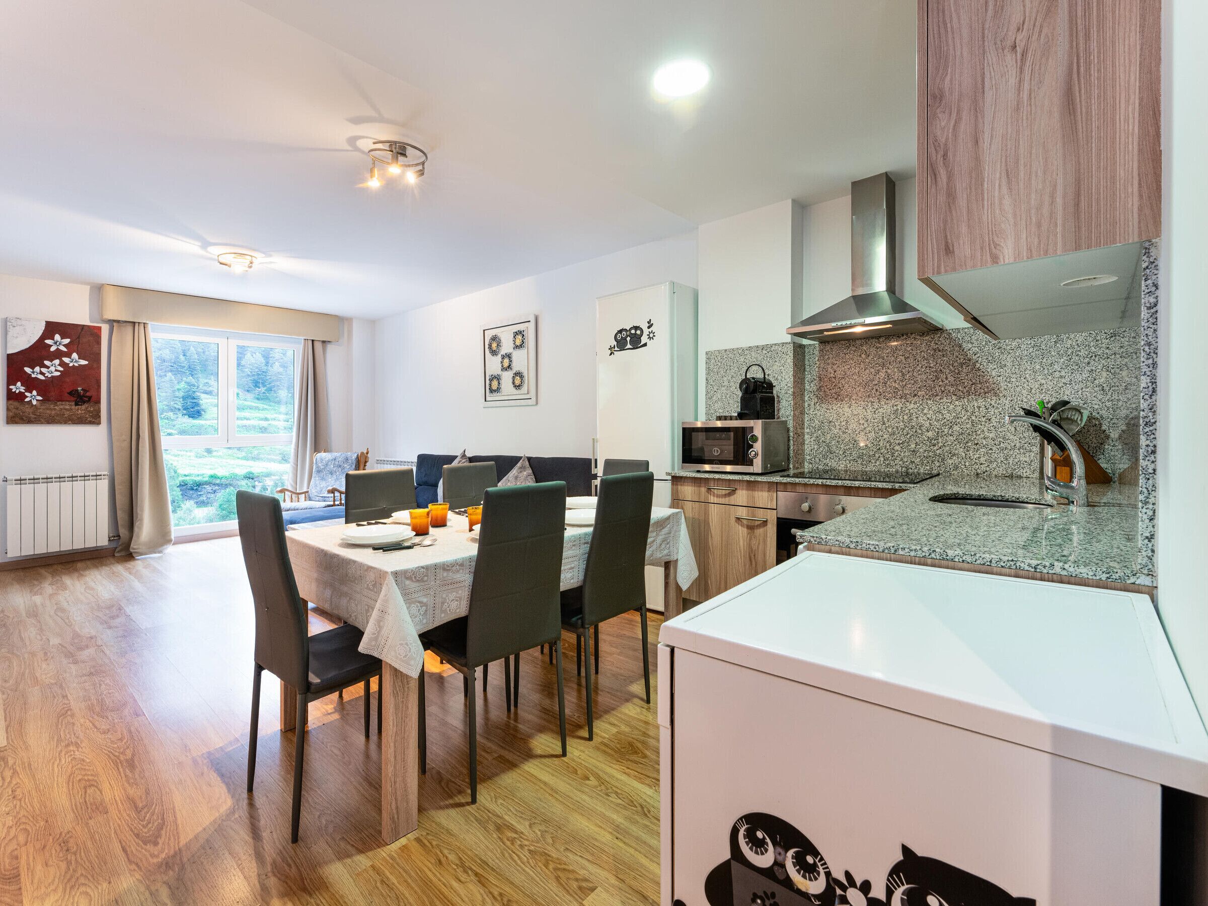 Een moderne keuken met een eetgedeelte, houten vloeren en uitzicht op een tuin door het raam.