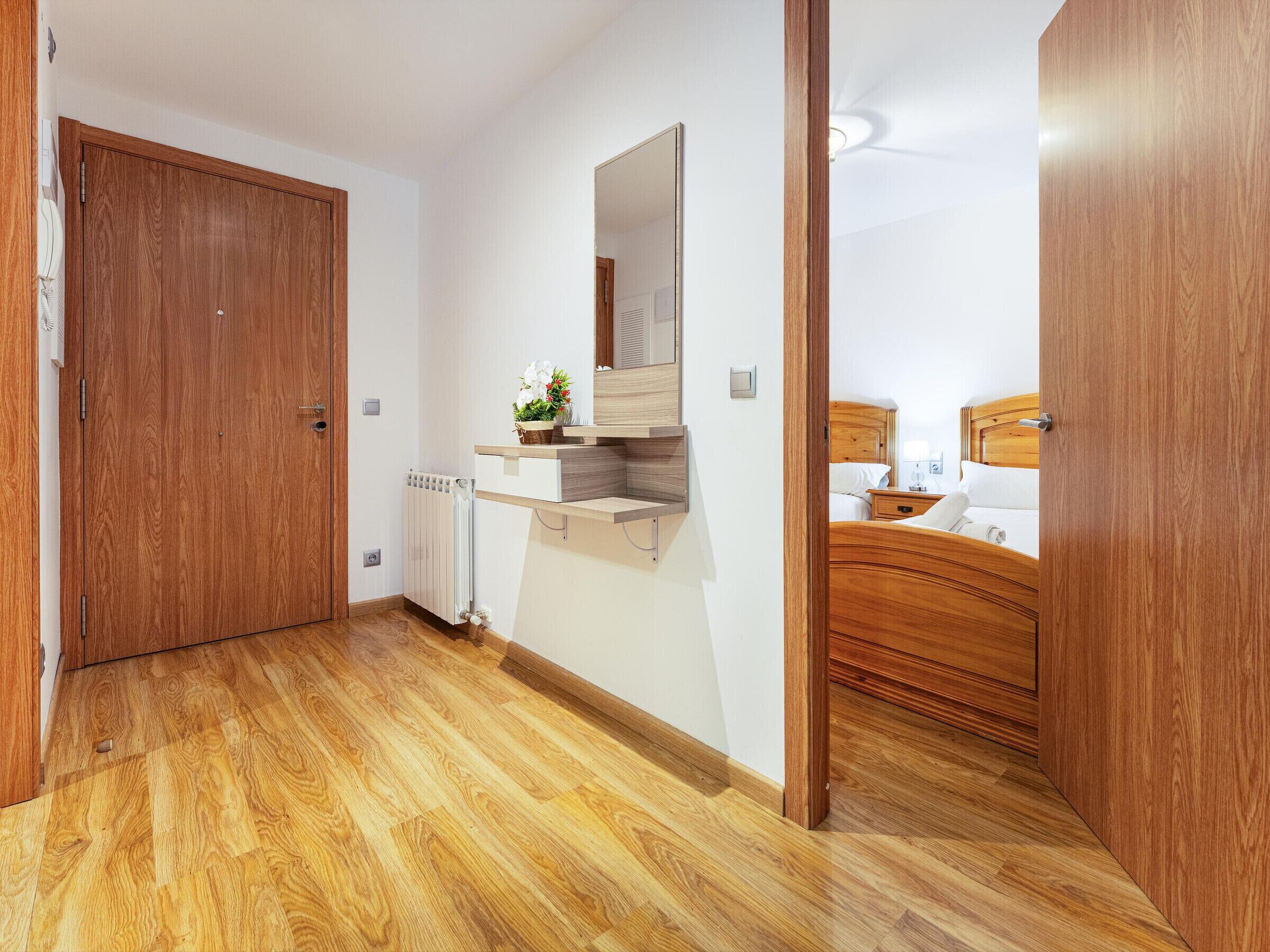 Habitación de hotel con suelo de madera, un armario de madera, estante empotrado con espejo y cama con cabecera de madera.