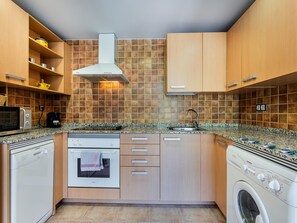 A compact kitchen with wooden cabinets, a microwave, a stove, and a washing machine. - Modern apartment with panoramic view - 4 guests (El Tarter)