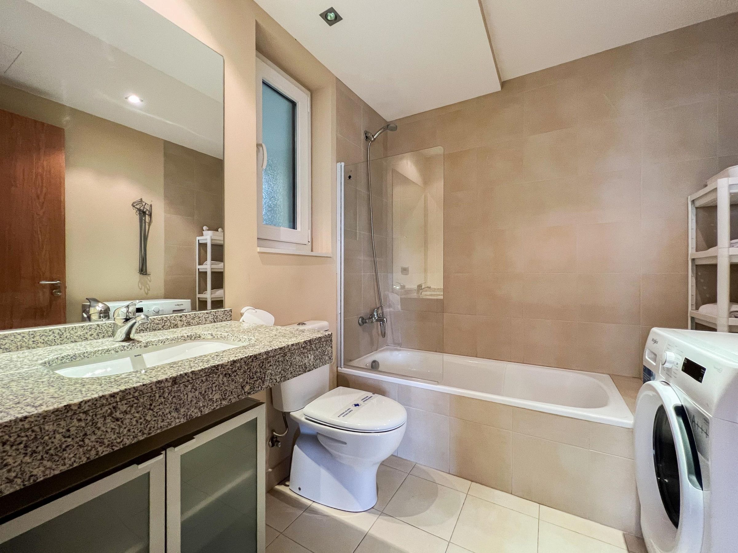 Une salle de bain moderne avec un comptoir en granit, des toilettes, une baignoire et un lave-linge.