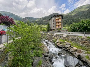 En bygning i sten med flere balkoner med udsigt over en bugtende å og frodig vegetation.