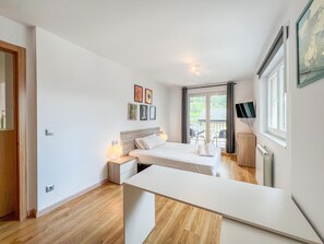 Ein modernes Schlafzimmer mit Bett, Nachttischen, einem Schreibtisch und einem Balkon mit Sitzgelegenheiten.