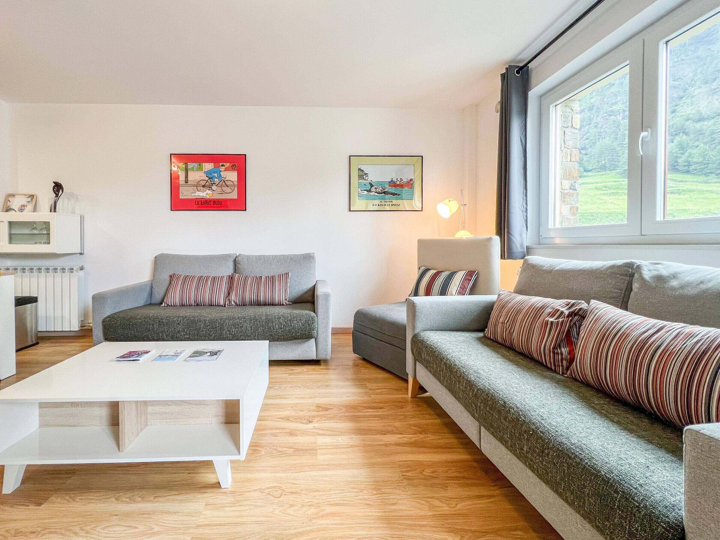 Een moderne woonkamer met twee grijze banken, een witte salontafel en een lamp. Er hangen twee ingelijste foto’s aan de muur.
