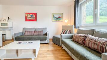 Een moderne woonkamer met twee grijze banken, een witte salontafel en een lamp. Er hangen twee ingelijste foto’s aan de muur.