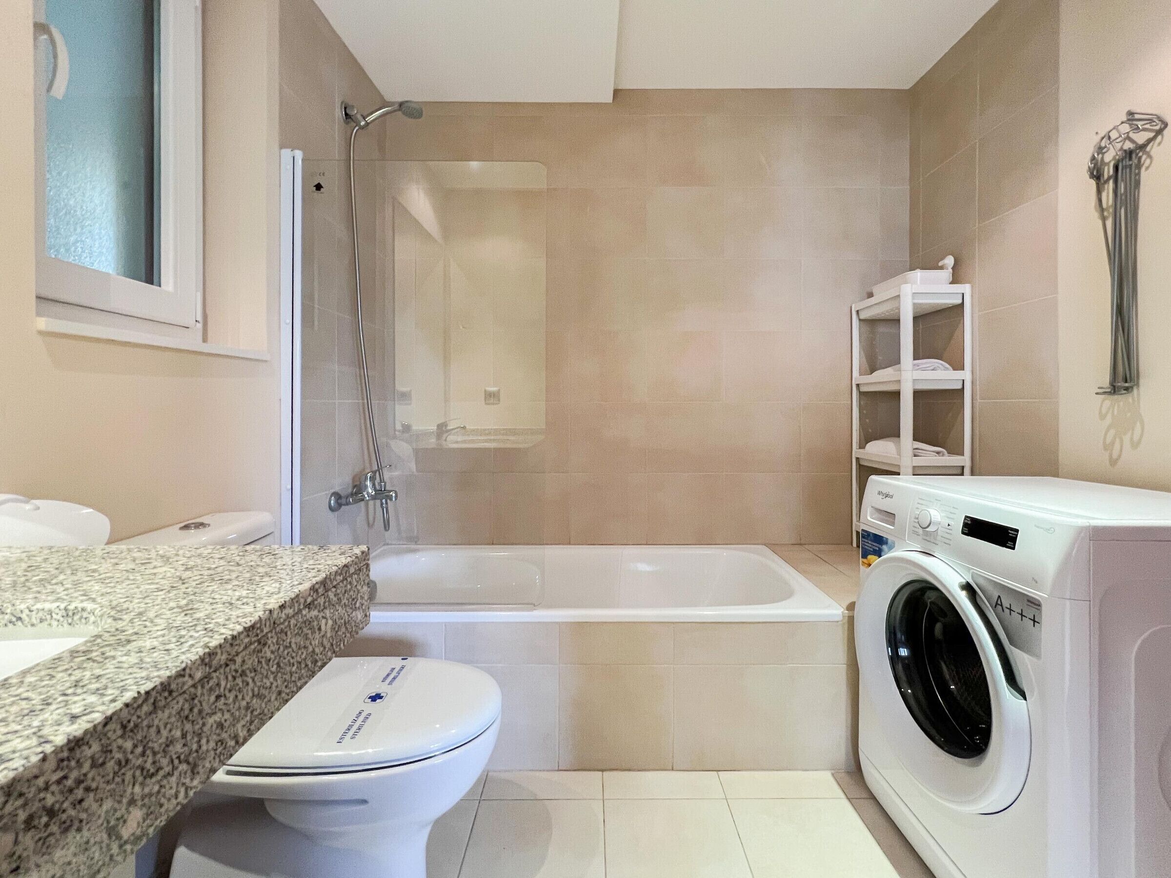 Une salle de bain équipée d’une baignoire, de toilettes, d’un lave-linge et d’une étagère avec des serviettes.