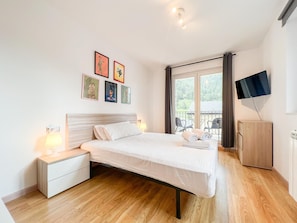 Et soveværelse med seng, sengeborde, fjernsyn og en balkon med stole.
