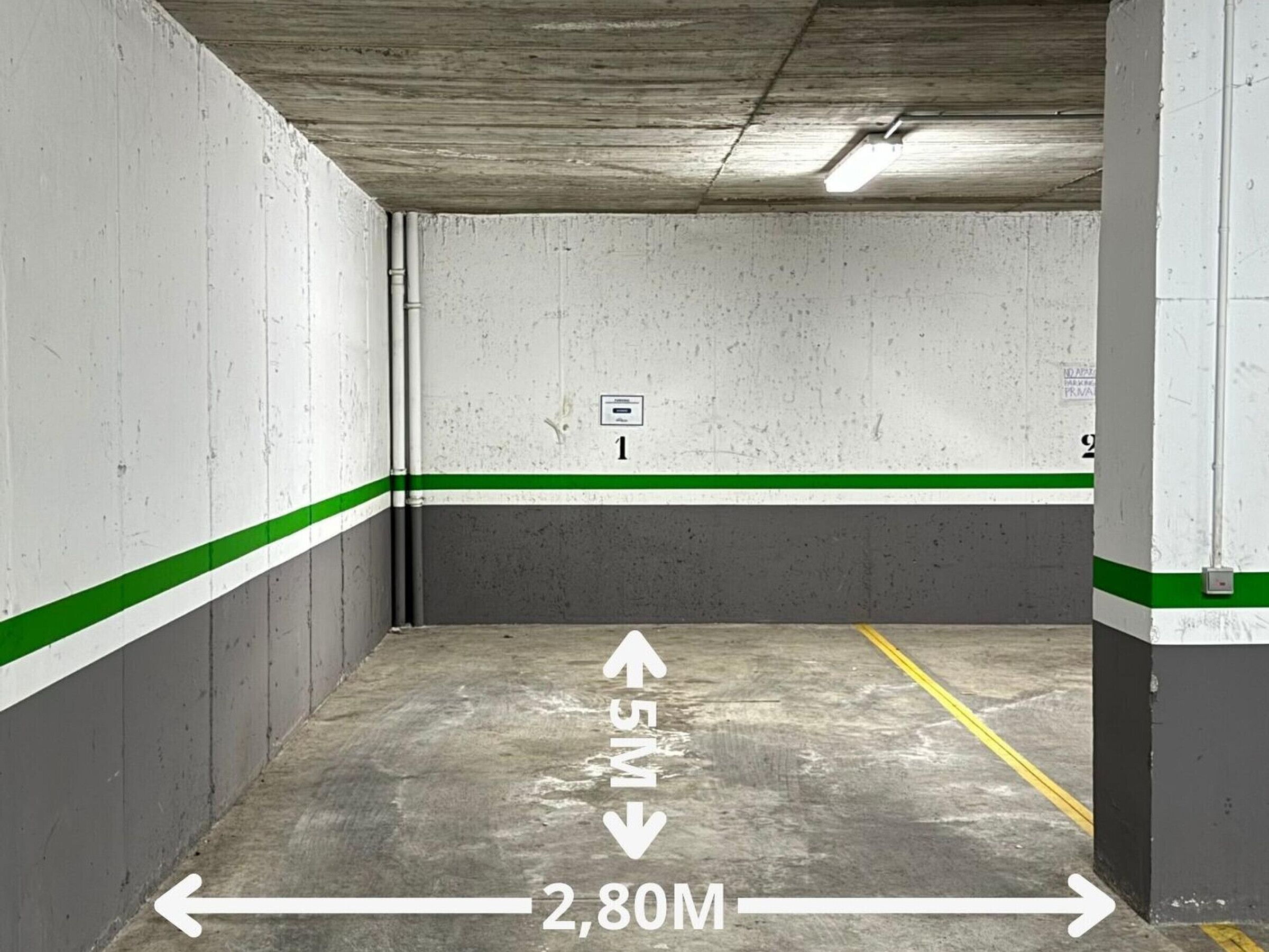 An empty parking garage with concrete walls, green and white stripes, and directional arrows indicating parking spots.