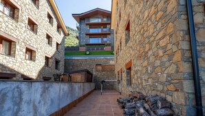 Un edificio de piedra con un patio empedrado, bancos de madera y una pila de leña.