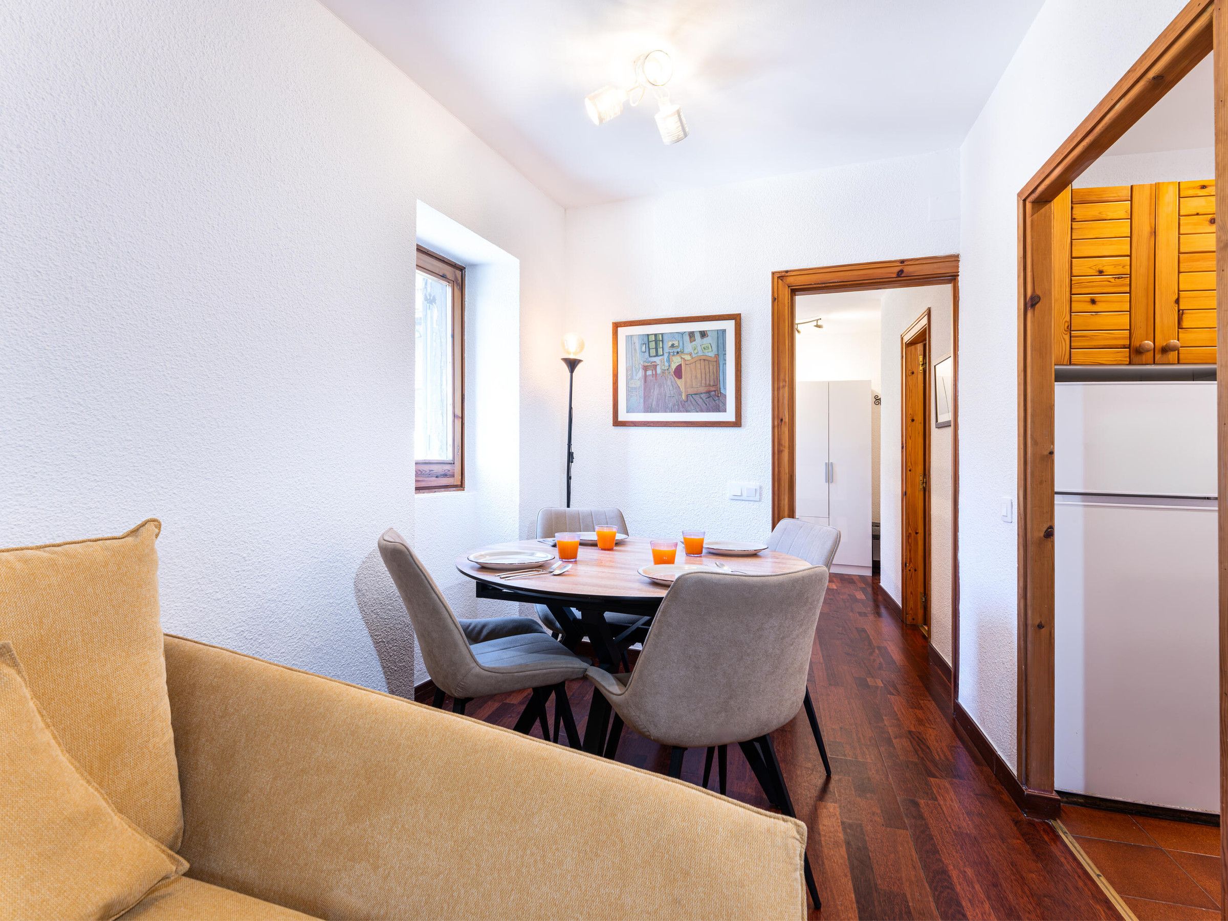 A dining area with a table, chairs, and a sofa. There is a refrigerator and a cabinet in the background.