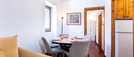Un comedor con una mesa, sillas y un sofá. Se observa un refrigerador y un armario al fondo.