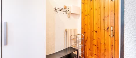 A wooden door with a metal handle, a white wall with a thermostat, and a metal shelf with a basket.