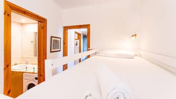 Habitación de hotel con cama, lavadora, espejo y baño con lavamanos y ducha.