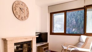 Ein Wohnzimmer mit Kamin, Fernseher, Sofa, Couchtisch und einer großen Wanduhr.