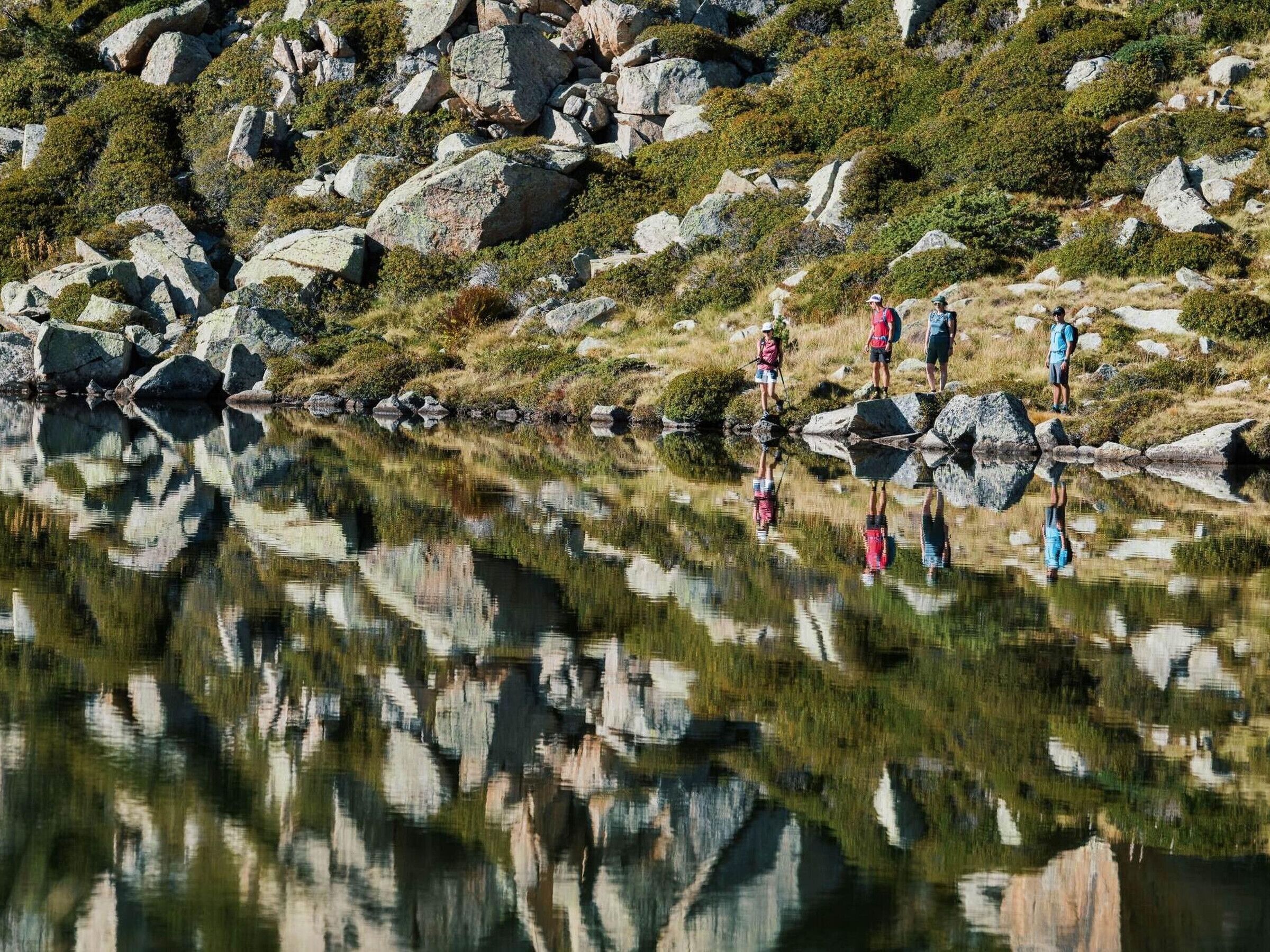 A group of people standing on rocks near a reflective body of water, surrounded by a rocky landscape.