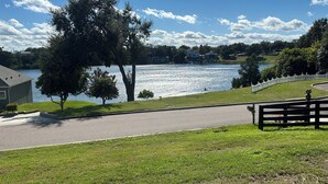 Vista al lago con un sendero pavimentado, un banco y una zona verde.