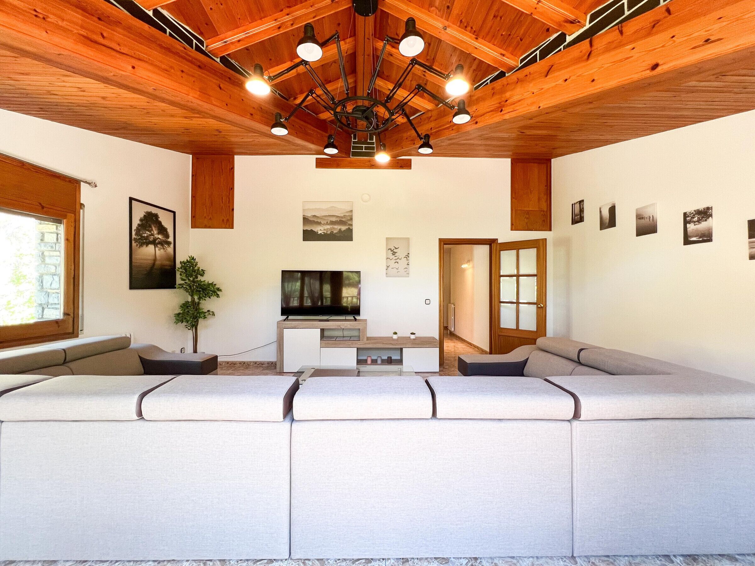 Una sala de estar moderna con techo de madera, un sofá grande, un televisor y una planta.