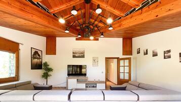 A modern living room with a wooden ceiling, a large sofa, a television, and a plant.