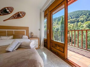 A bedroom with a large bed, a nightstand, a lamp, and a view of a forested hillside through a balcony. - Rider Apartment - 8 Guests, 4 Bedrooms (Pal)