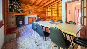 A wooden interior with a fireplace, a dining table with chairs, and a large window. - Rider Apartment - 8 Guests, 4 Bedrooms (Pal)