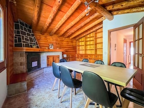 A wooden interior with a fireplace, a dining table with chairs, and a large window.
