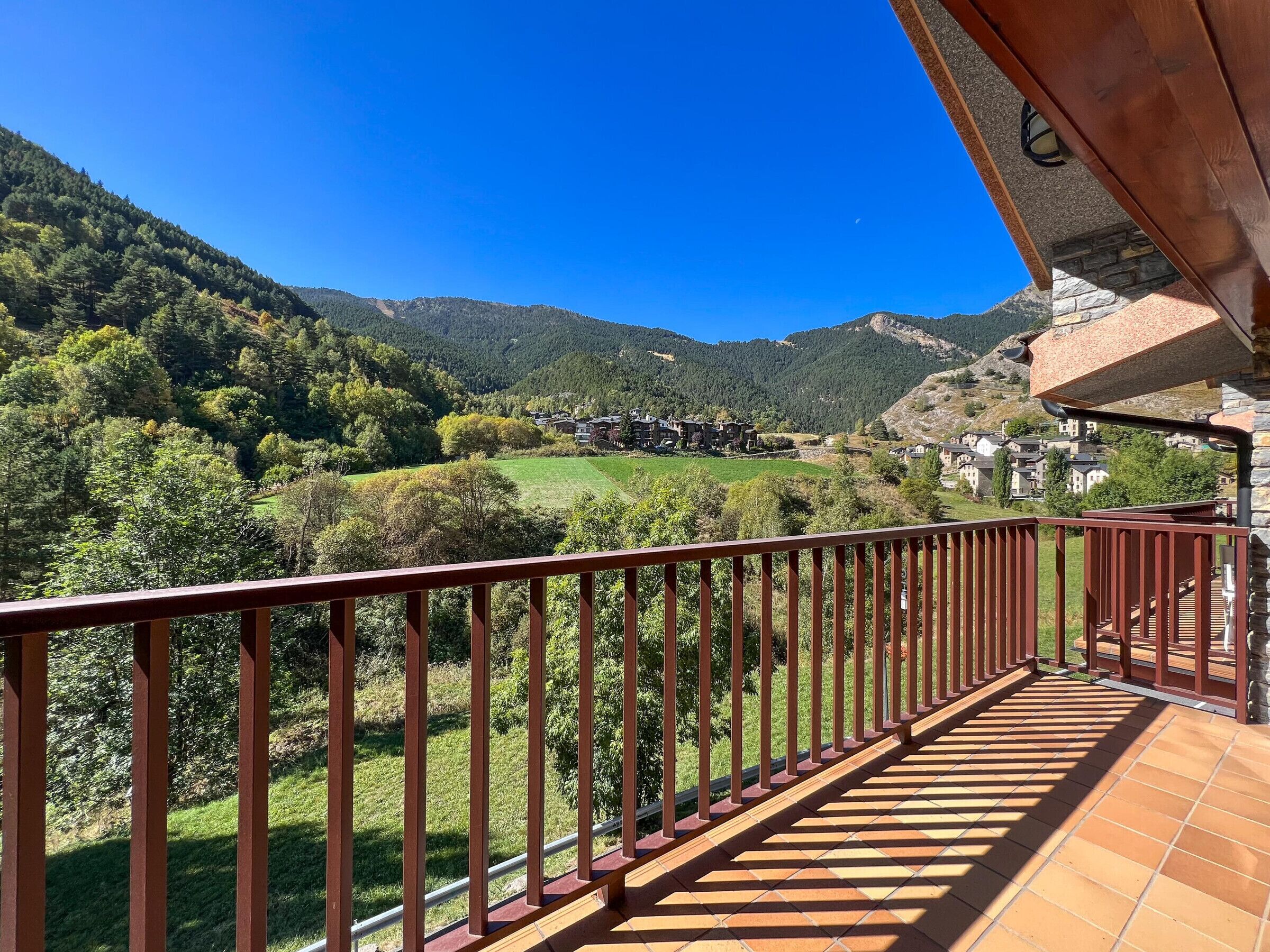 Un balcón con barandilla de metal que da a un paisaje montañoso con casas.