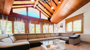A modern living room with a sectional sofa, a glass coffee table, and large windows offering a view of the outdoors. - Rider Apartment - 8 Guests, 4 Bedrooms (Pal)
