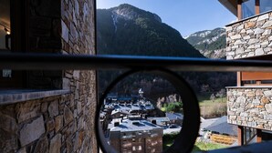 Blick durch ein rundes Fenster auf ein Bergdorf mit Steinhäusern und einer Kirche.