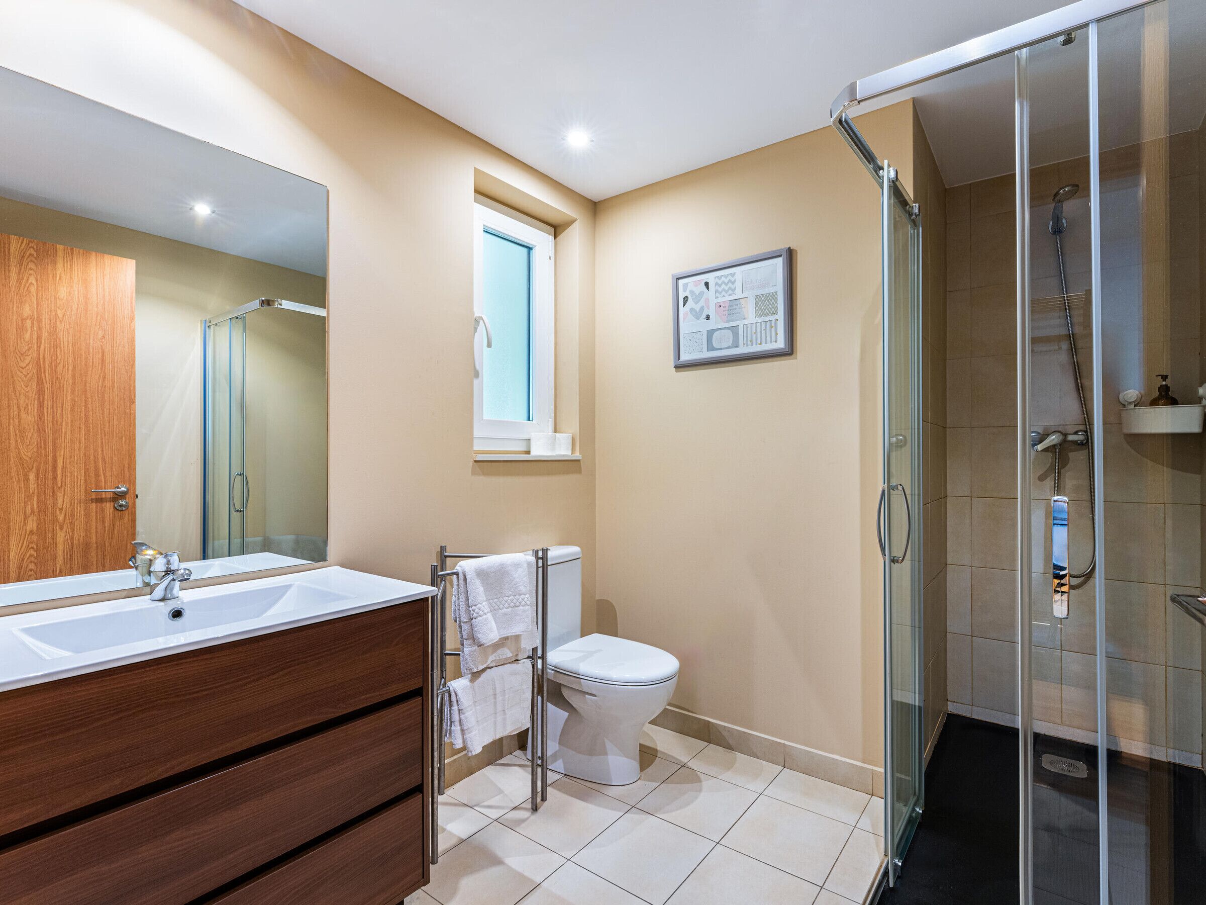 A bathroom with a wooden vanity, a glass shower enclosure, and a toilet.
