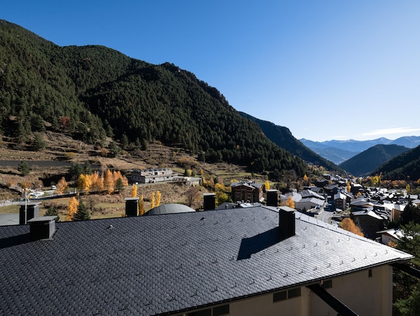 Un village de montagne aux bâtiments traditionnels, sous un ciel dégagé, et entouré d’un feuillage automnal.