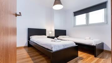 Een moderne slaapkamer met twee bedden, een houten vloer, een raam met zonwering en een hanglamp.