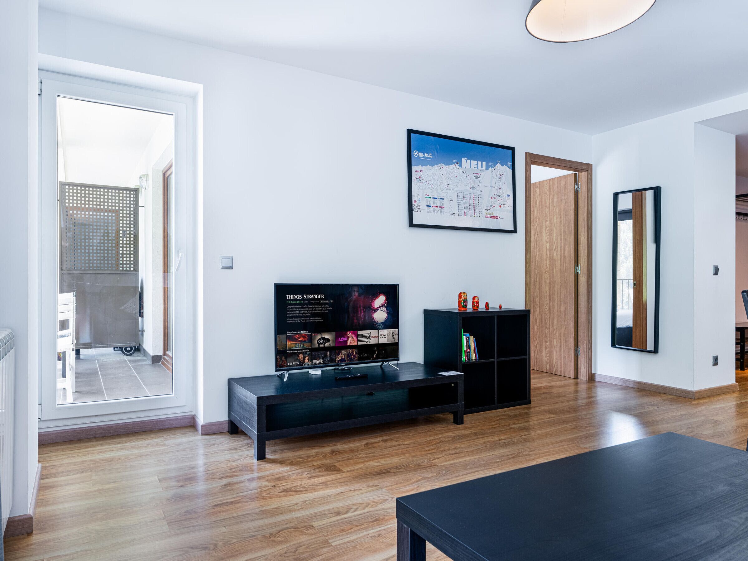 Una sala de estar moderna con un televisor de pantalla plana, piso de madera, un mueble de entretenimiento negro y un mapa grande enmarcado en la pared.