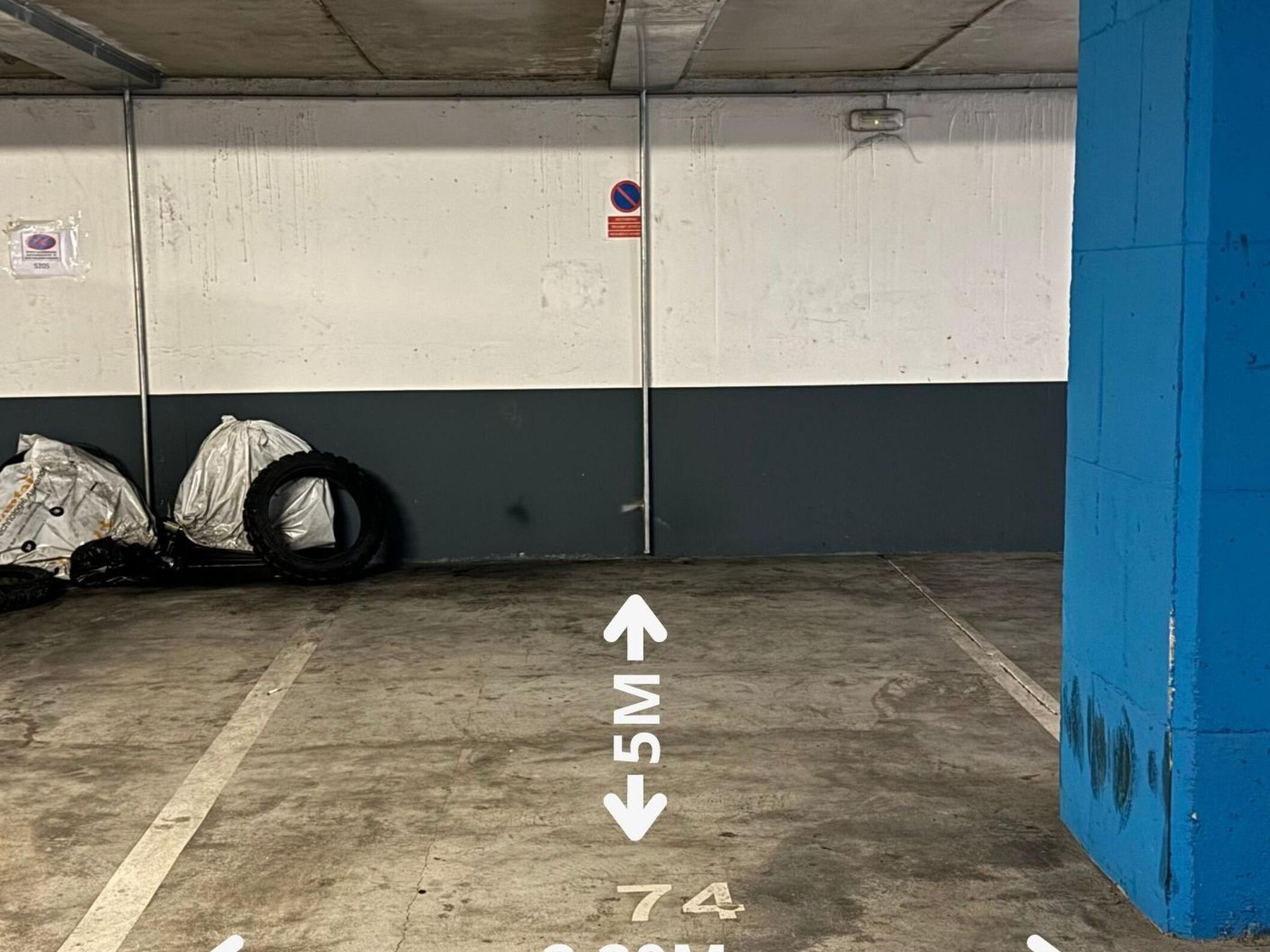 Un estacionamiento con paredes de hormigón, un pilar azul y una flecha direccional en el suelo.