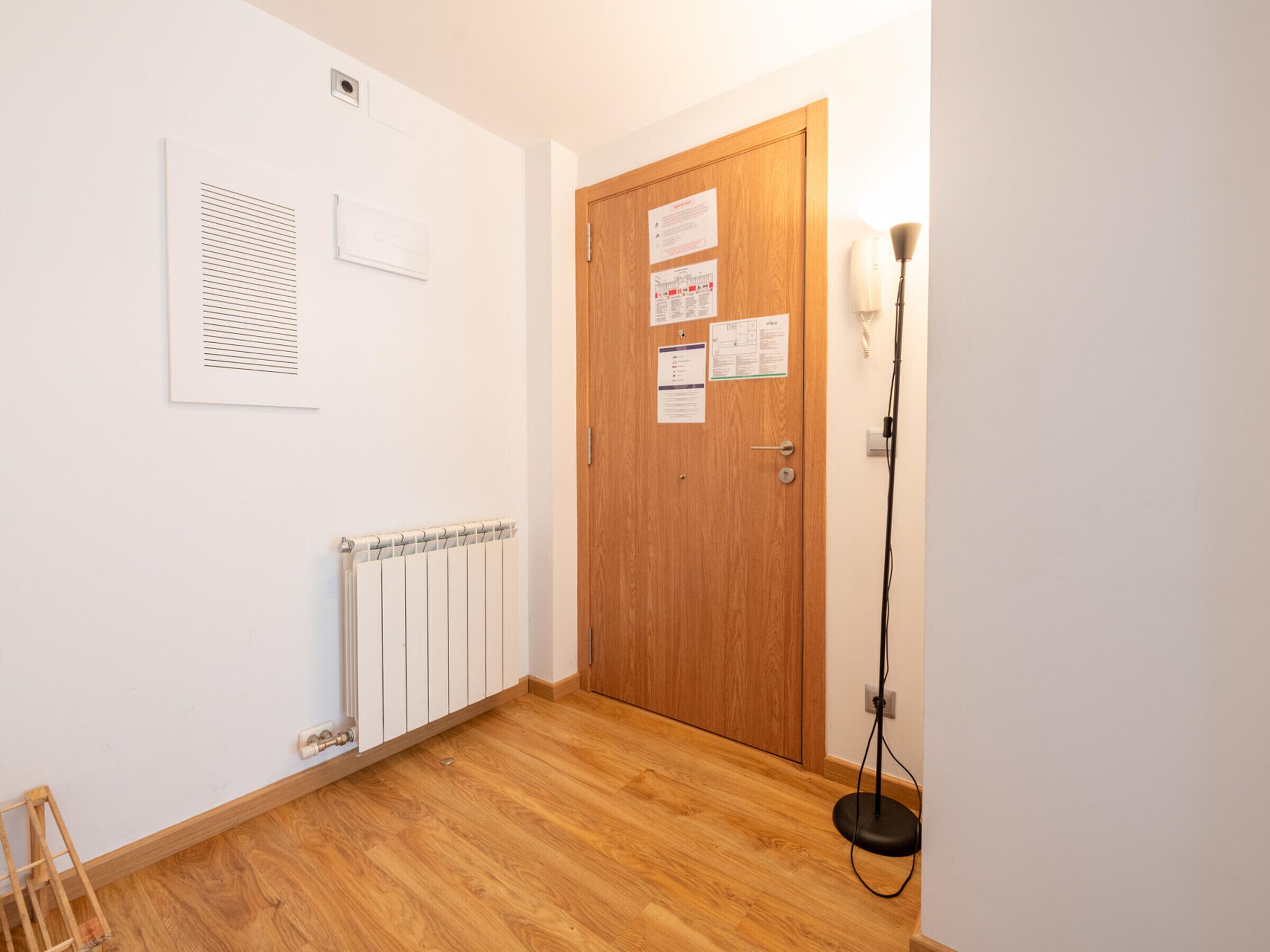 Un pasillo con puerta de madera, un radiador y una lámpara de pie.