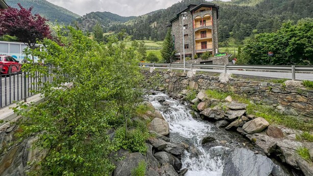 Ein Steinhaus mit mehreren Balkonen, das auf einen Fluss und üppiges Grün blickt.