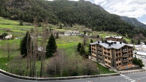 Ein Gebäude mit einer Steinfassade und mehreren Balkonen, umgeben von einer üppigen grünen Landschaft und Bergen im Hintergrund.