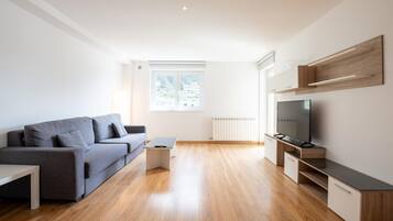 A modern living room with a grey sofa, a TV, and wooden flooring.