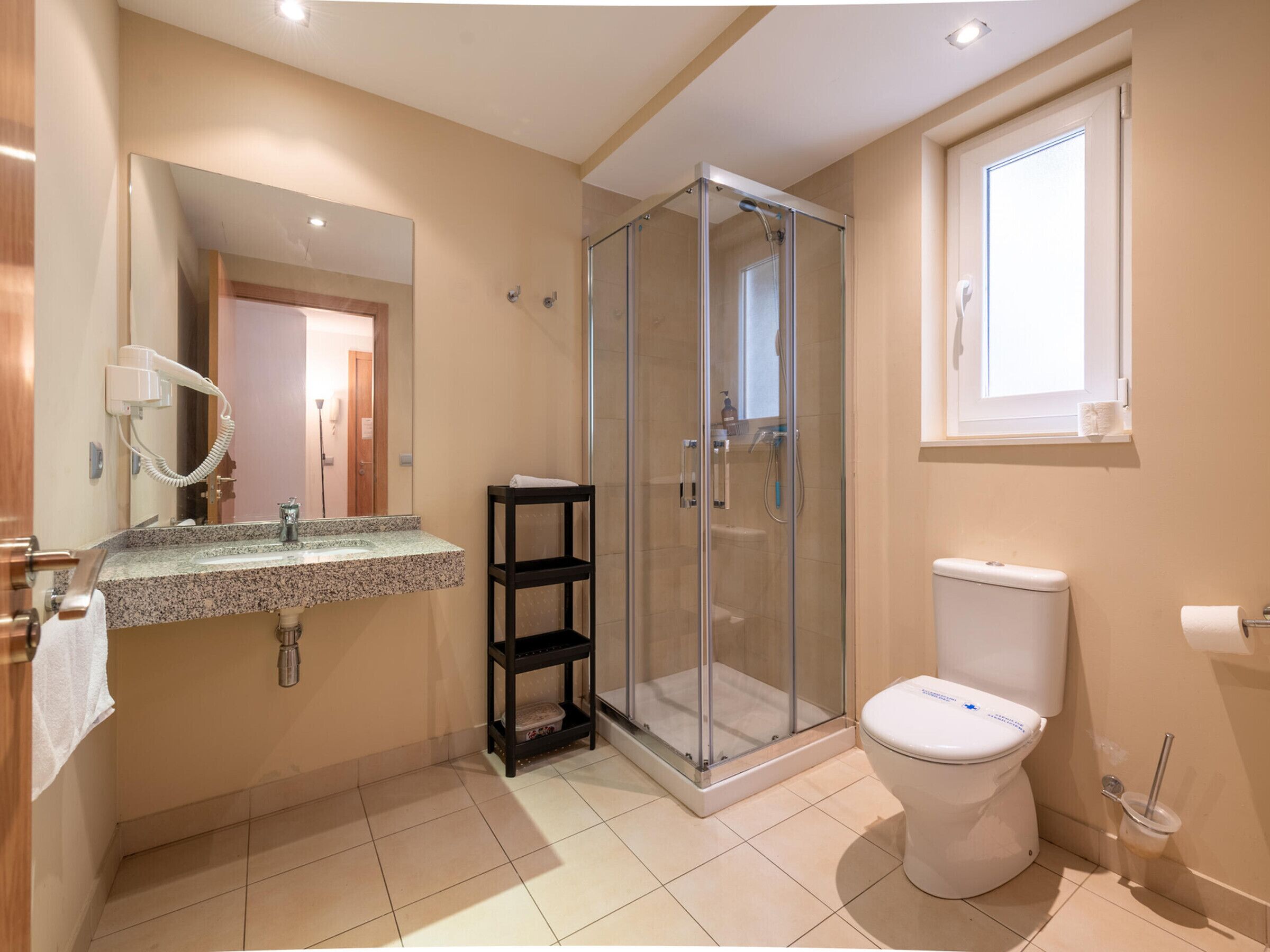 Een badkamer met een douchecabine van glas, toilet, wastafel met spiegel en raam.